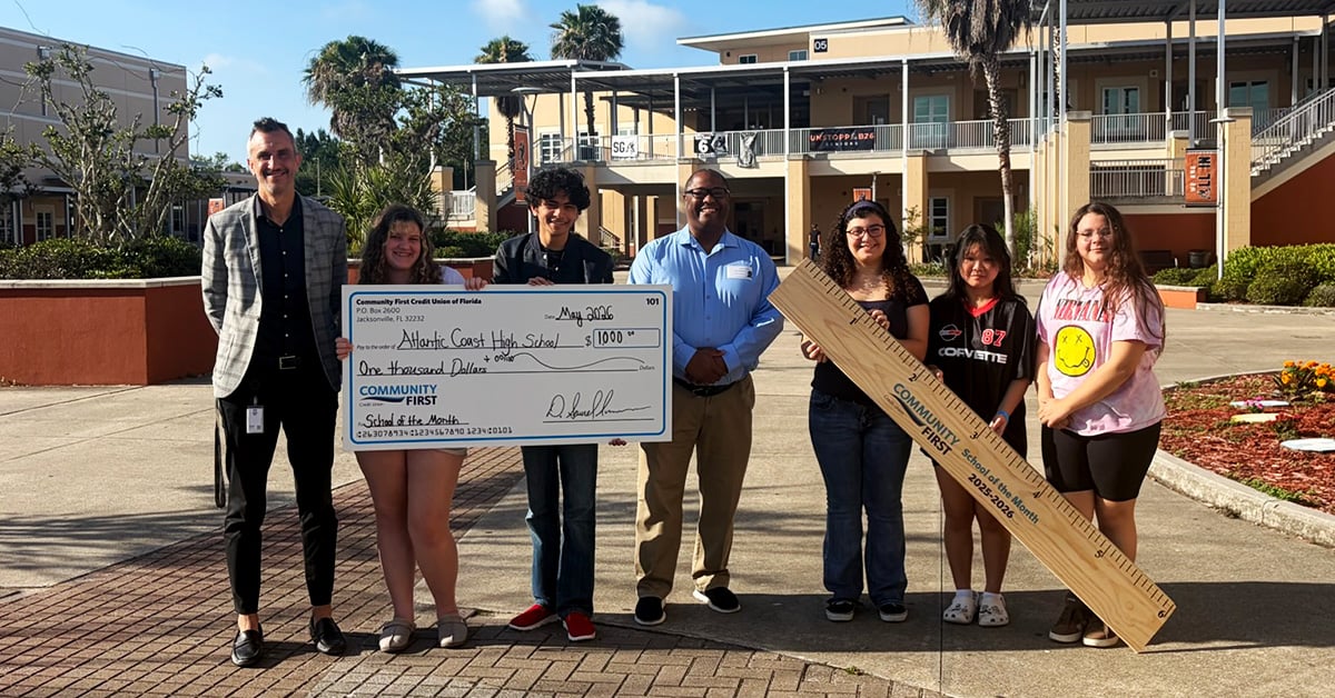 Teachers and students with big check and oversized ruler.