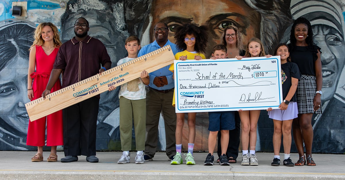 Teachers and students with big check and oversized ruler.
