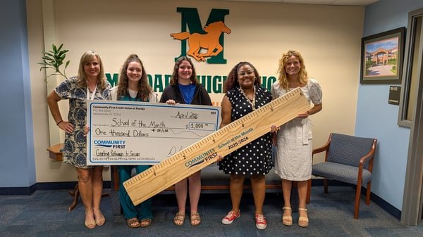 Teachers with big check and oversized ruler.