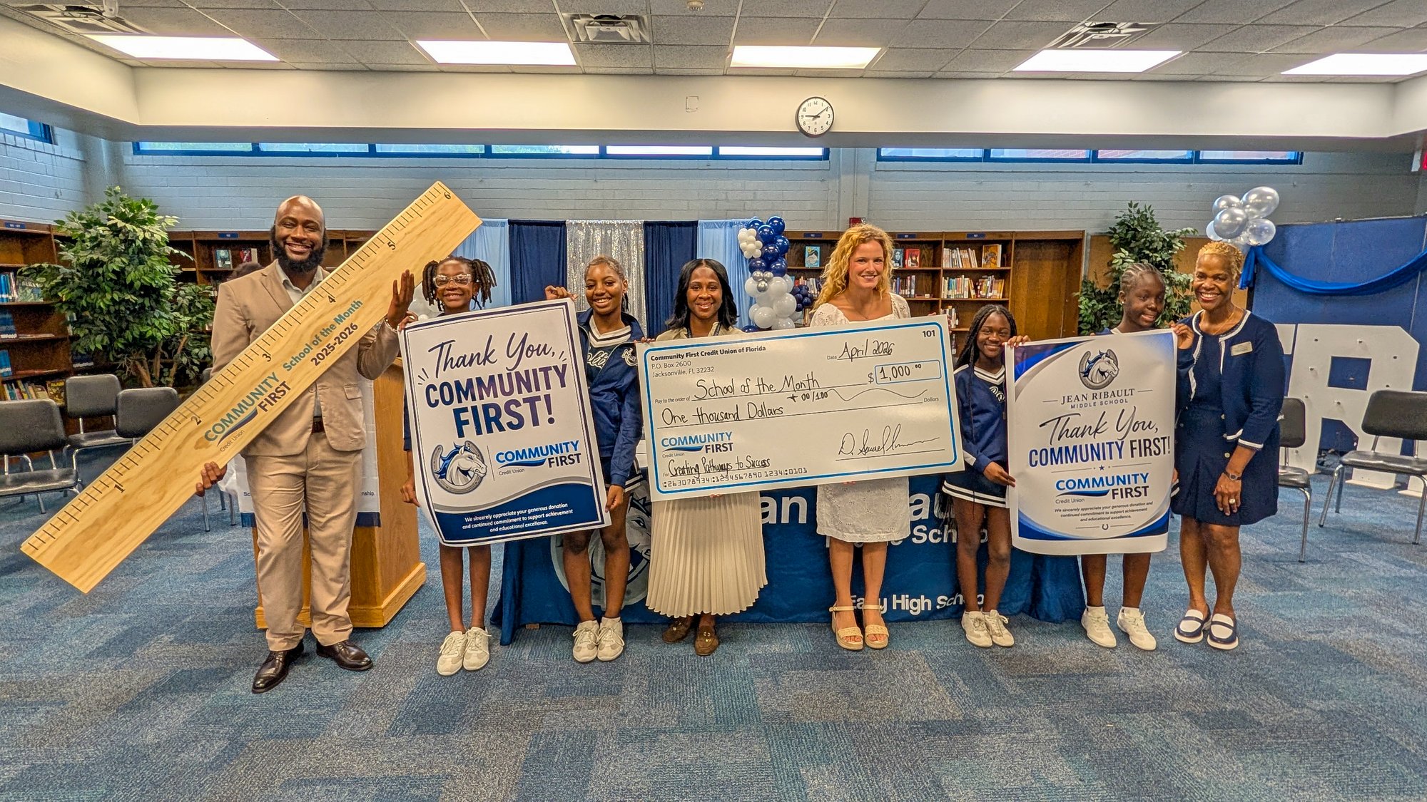 Students with giant ruler, big check and sign.