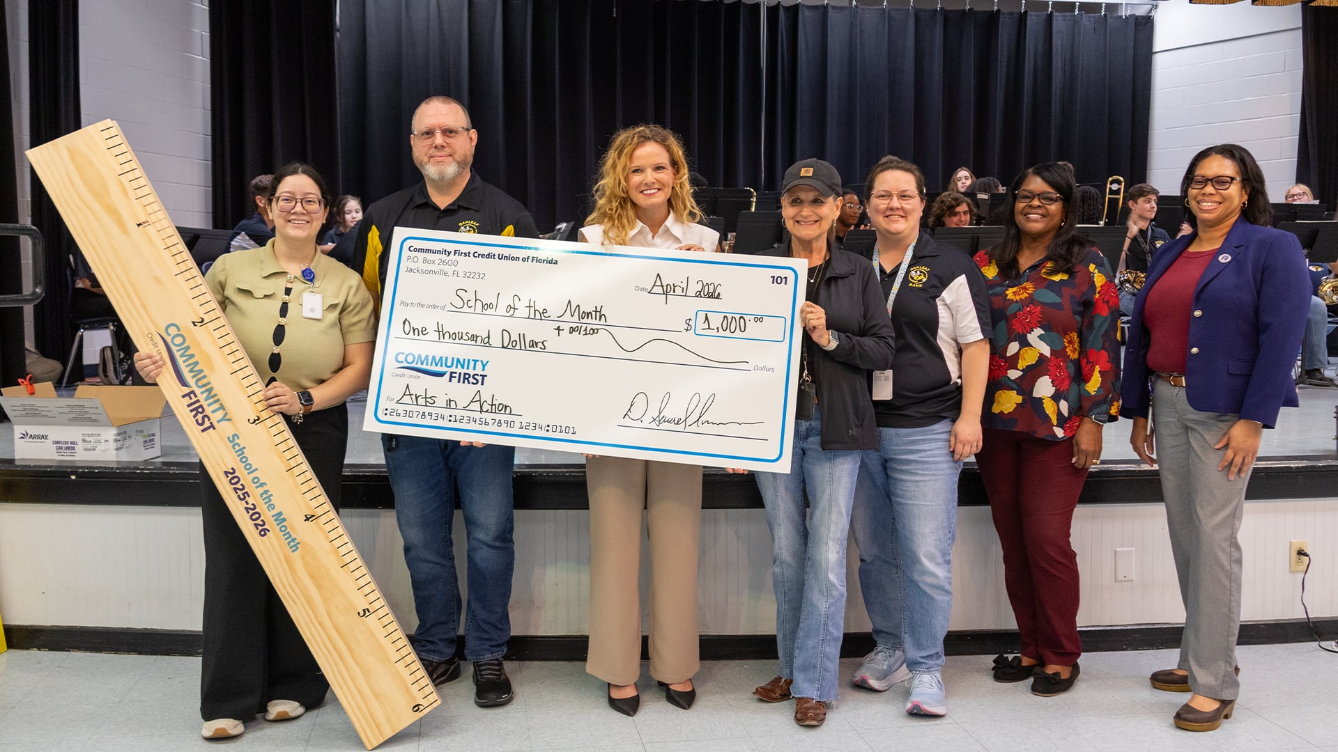 Teachers smiling with giant ruler and big check.