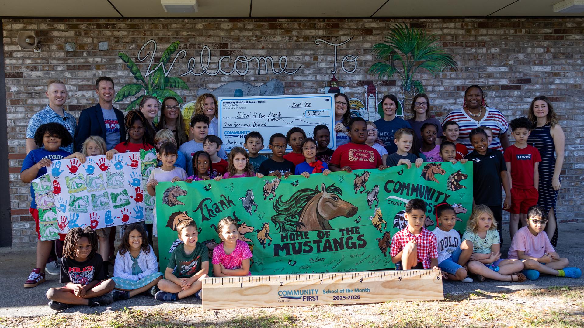 Students posing with a giant ruler, poster and big check.