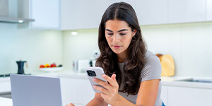 Woman looking at phone while on laptop.